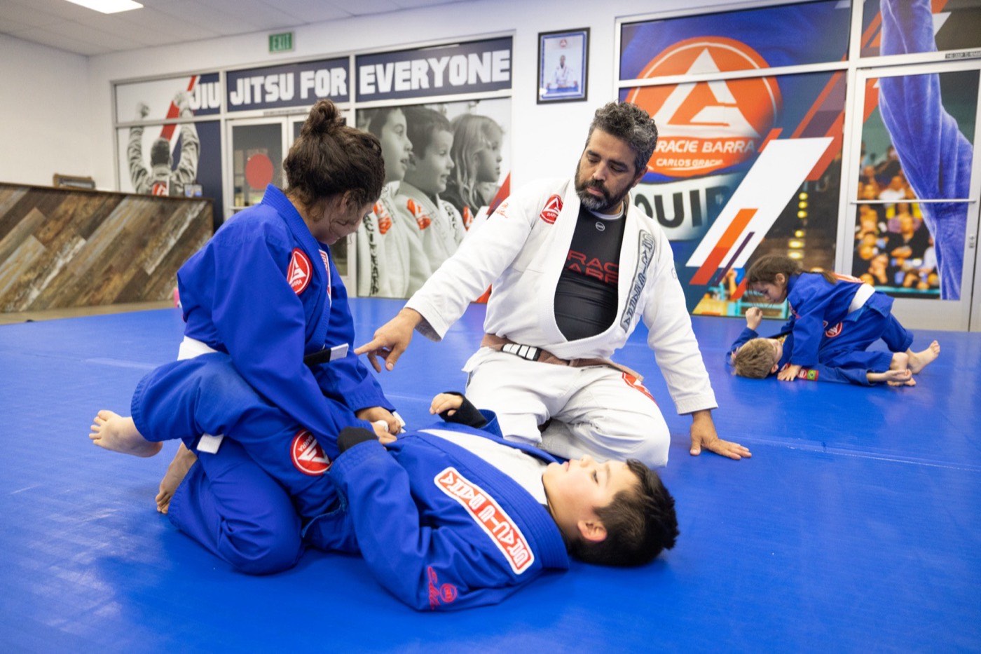 An instructor kneels beside two kids practicing a position