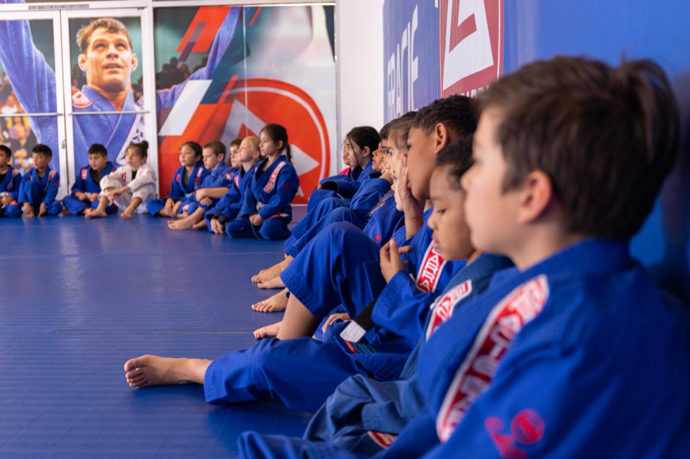A row of kids sits shoulder to shoulder listening to their instructor